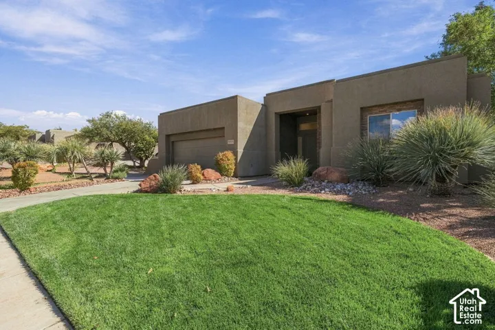 Modern stucco exterior with an integrated garage, a window featuring stone detailing, and a xeriscaped front yard with mature desert landscaping