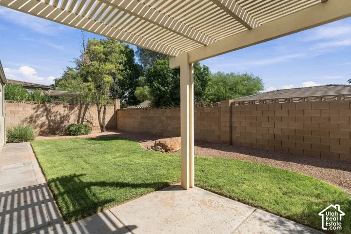 Expansive backyard featuring a slatted patio cover, concrete patio, grass lawn, and gravel landscaping