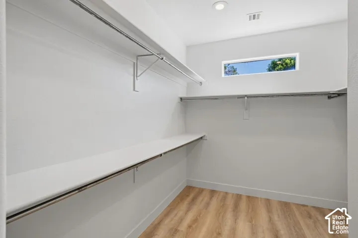 Walk-in closet featuring wood-finish flooring, recessed lighting, a horizontal window, and shelving with hanging rods