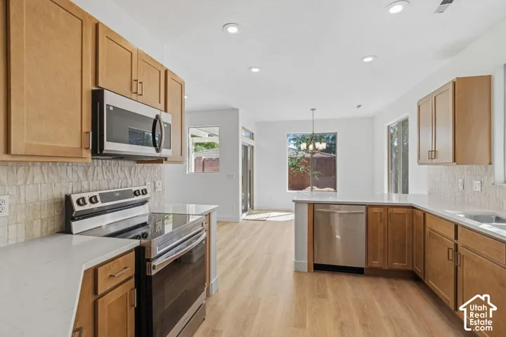Kitchen featuring wood-finish flooring, light wood cabinetry, stainless steel appliances, and solid surface countertops