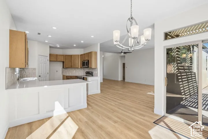 Kitchen island with white paneling and a light-toned countertop, wood-finish flooring, a sliding glass door with a transom window, and a contemporary chandelier