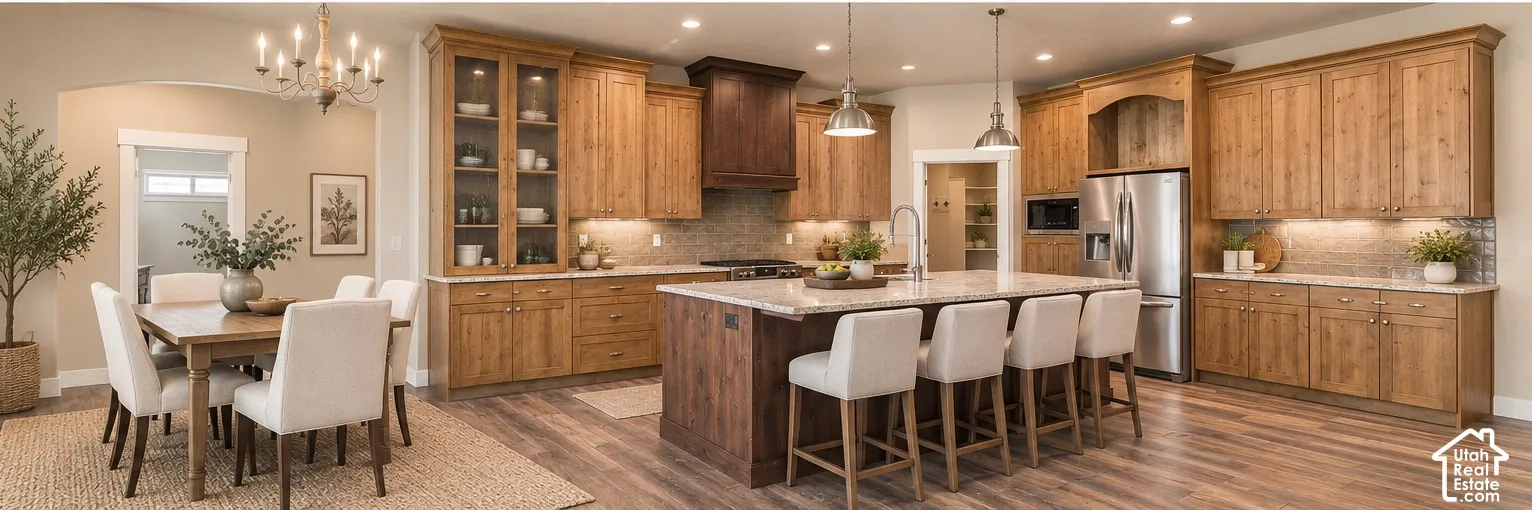 Kitchen featuring light wood-finish cabinetry, a large central island with a stone countertop, built-in stainless steel appliances, a custom range hood, and wood-finish flooring