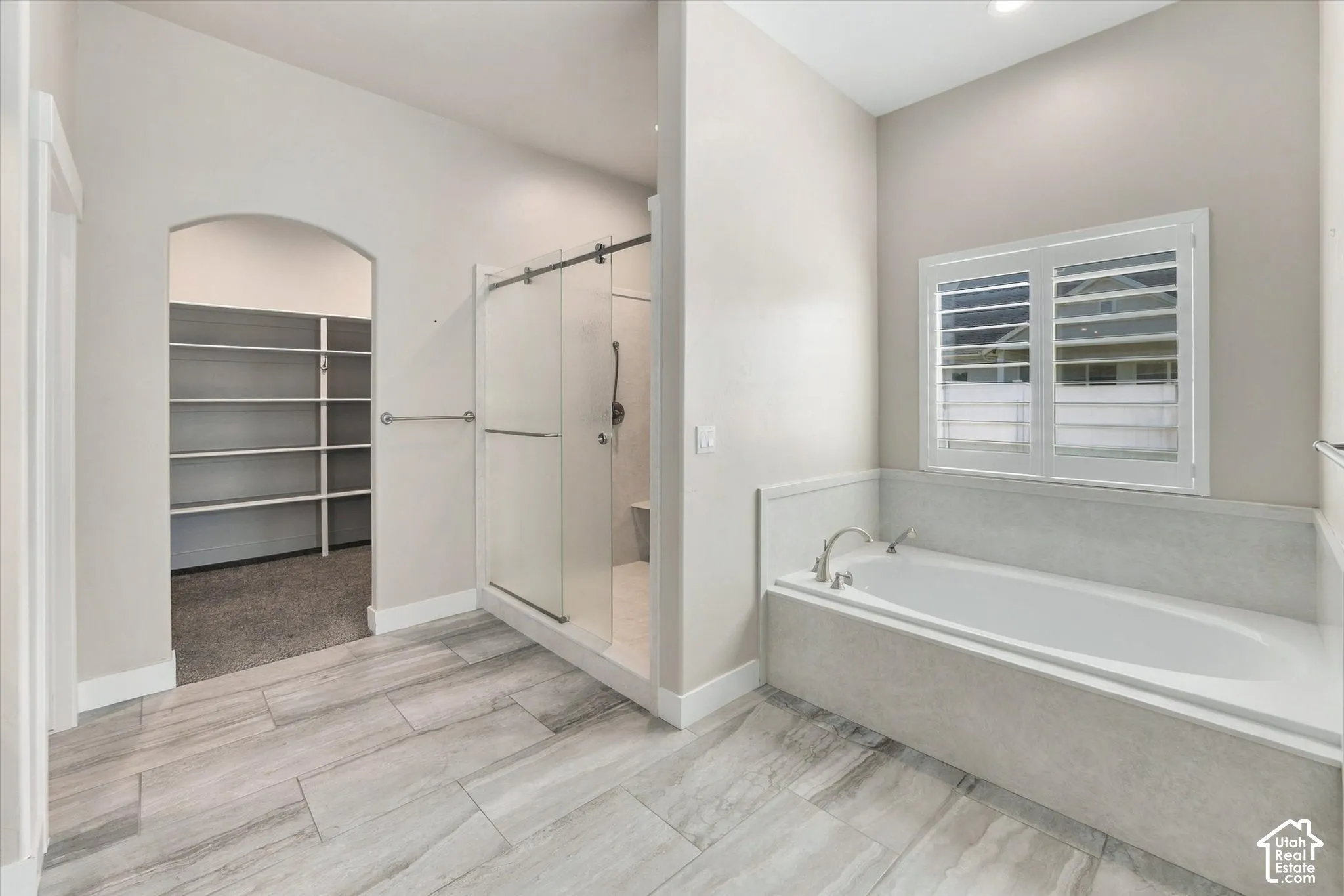 Master Ensuite  with Built-in soaking tub with plantation shutters, tiled shower and an arched entry to a walk-in closet with shelving