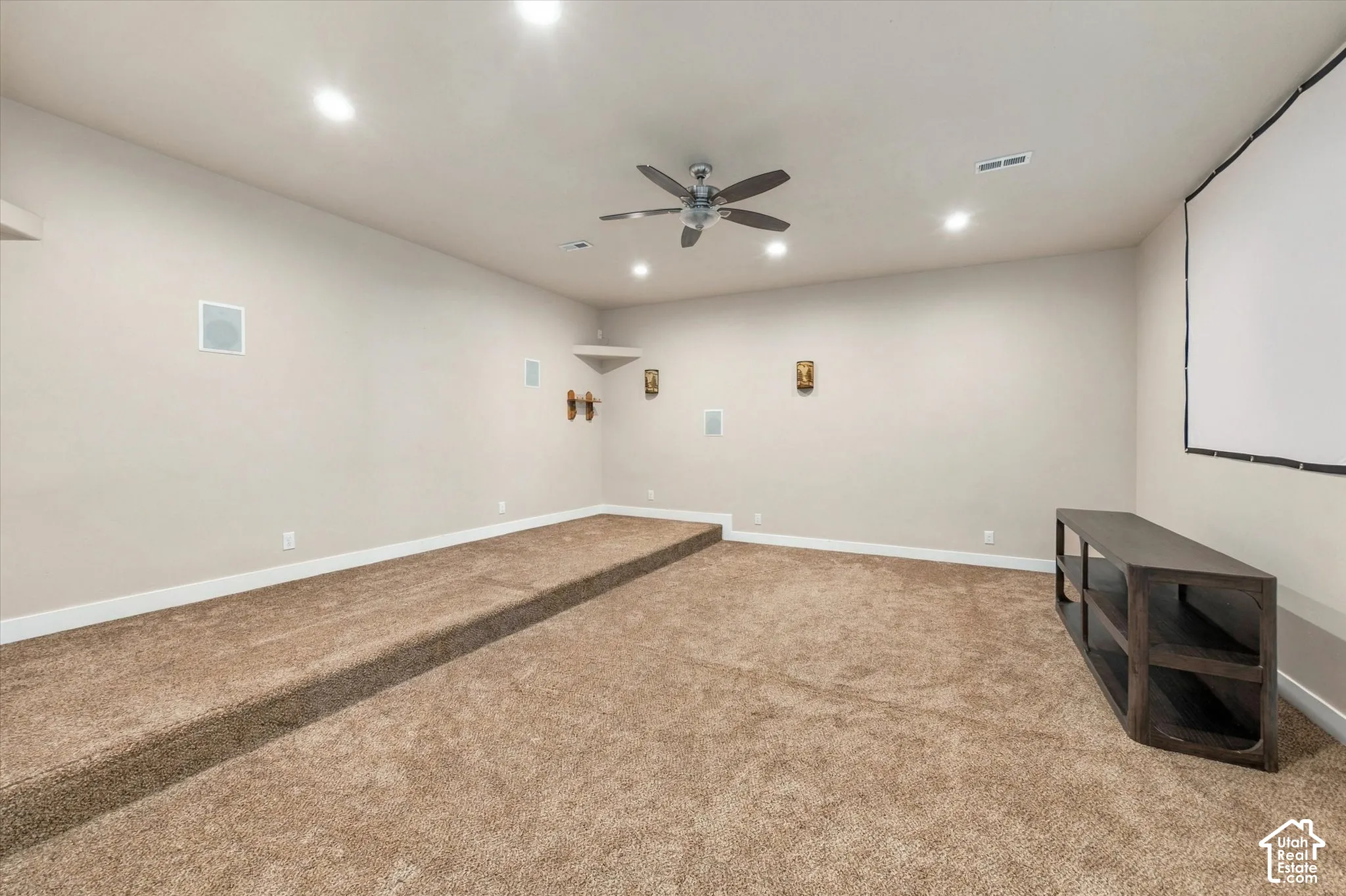 Carpeted room with a raised platform, recessed lighting, and ceiling fan