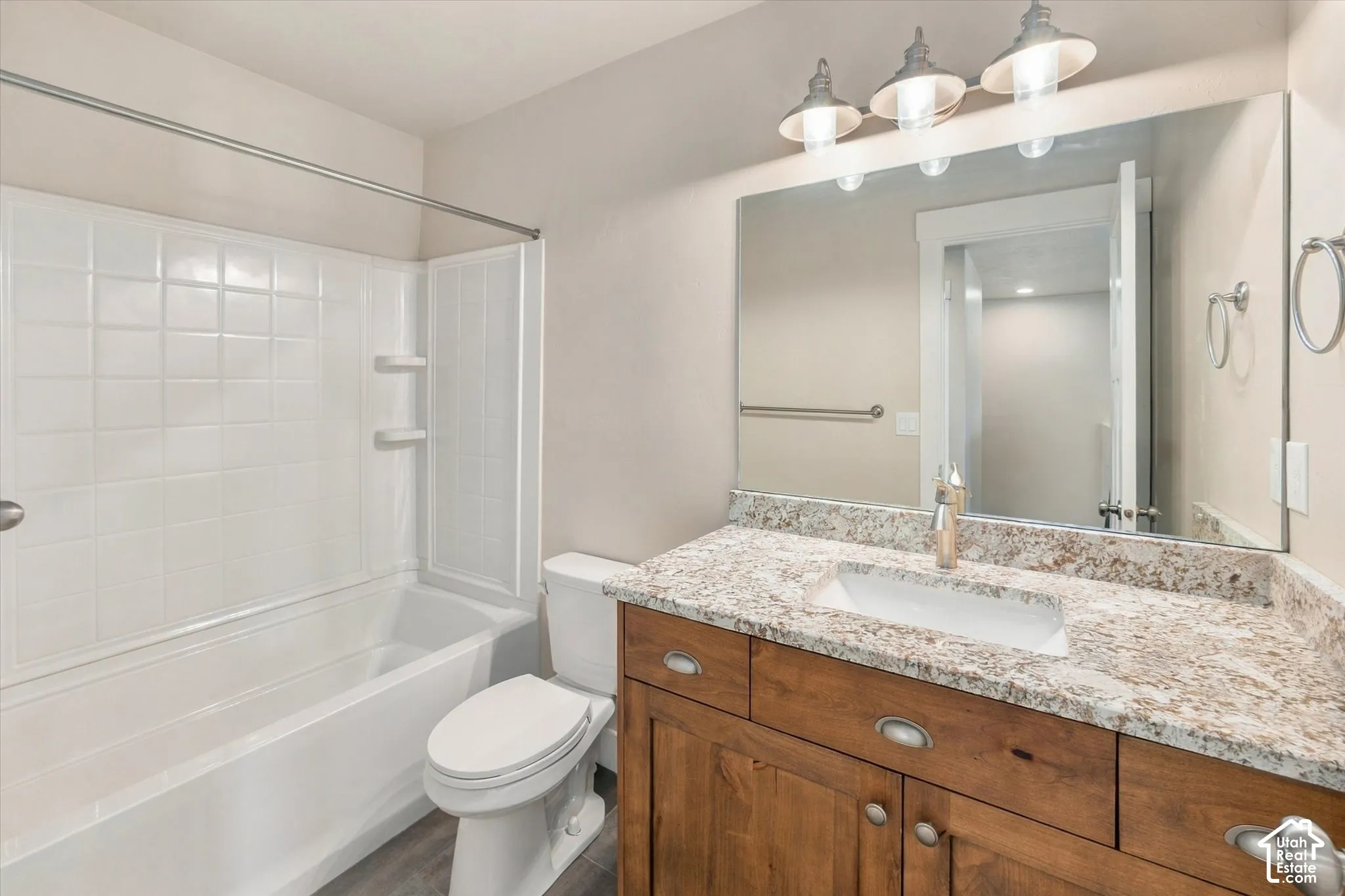Bathroom featuring a wood-finish vanity with stone-patterned countertop, integrated basin, three-light fixture, and tub-shower combination with full-height surround
