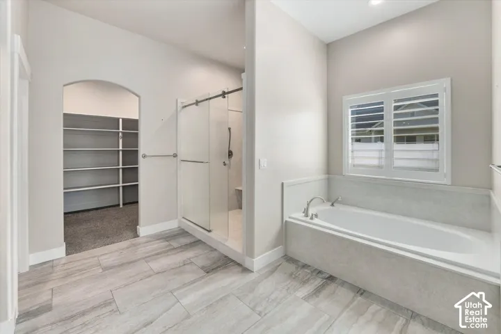 Master Ensuite  with Built-in soaking tub with plantation shutters, tiled shower and an arched entry to a walk-in closet with shelving
