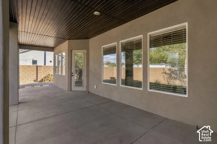 Covered outdoor patio with concrete flooring, stucco exterior, multiple windows, a glass-paneled door, and a privacy wall