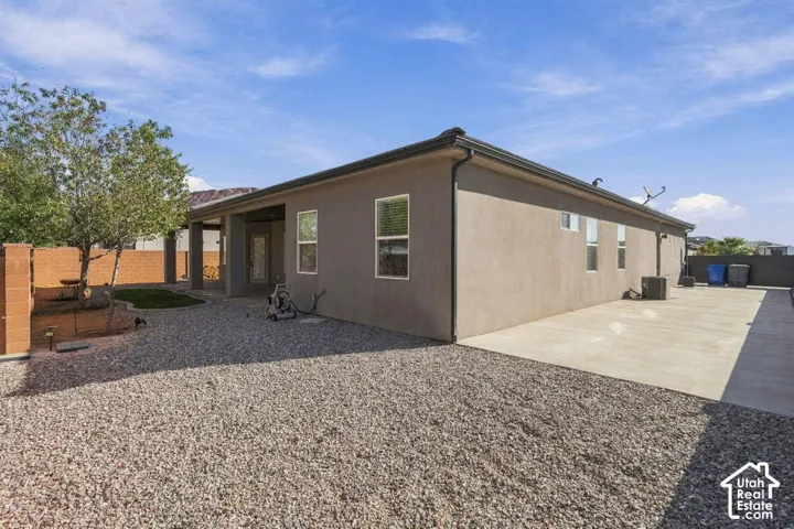 Stucco exterior with multiple windows, covered patio, gravel landscaping, and a concrete patio