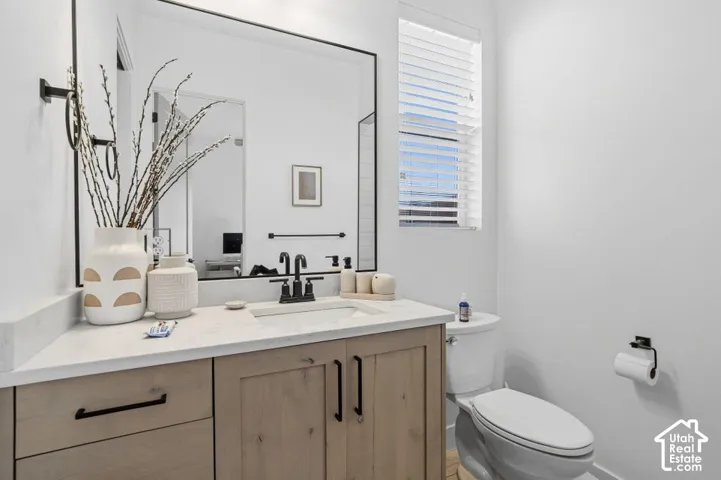 Single vanity with a light wood-finish cabinet and black hardware, topped with a light-toned countertop and an undermount sink