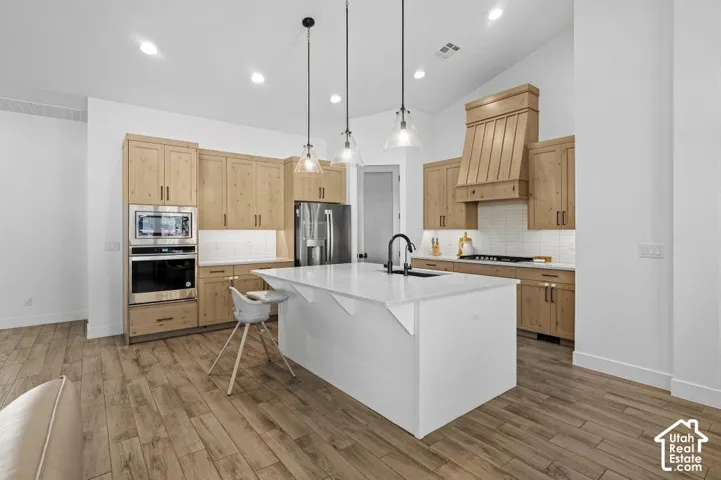 Kitchen featuring wood-finish flooring, a center island with a white countertop, light wood cabinetry, integrated stainless steel appliances, and pendant lighting