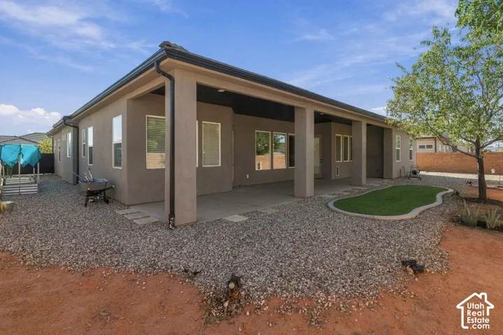 Rear exterior featuring a covered patio, gravel landscaping, and a shaped artificial turf area