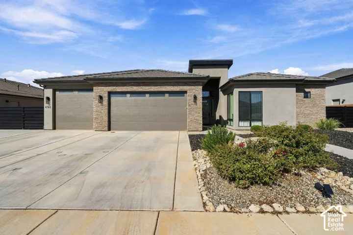 Stucco and stone facade with a multi-car garage, mature landscaping, and an extended driveway