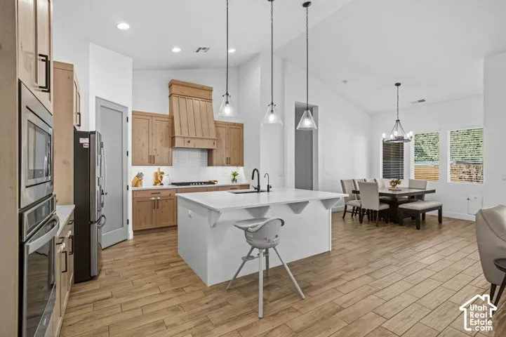 Open-concept kitchen and dining area featuring wood-finish flooring, a kitchen island with seating, pendant lighting, and stainless steel appliances