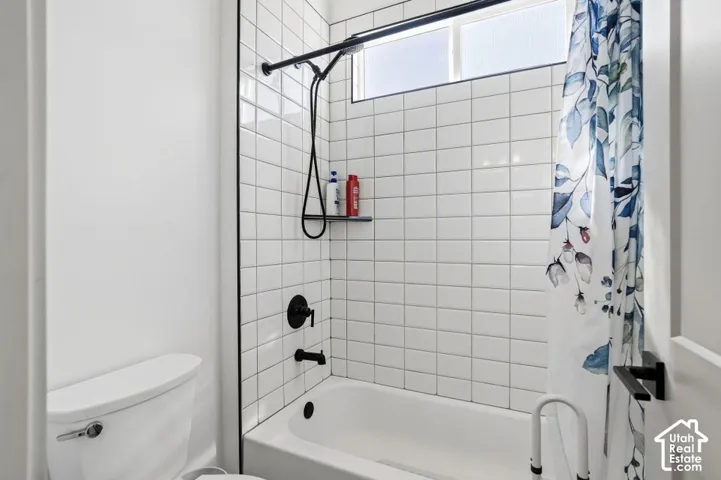 White subway tile surround with dark grout, matte black shower fixtures, and a transom window