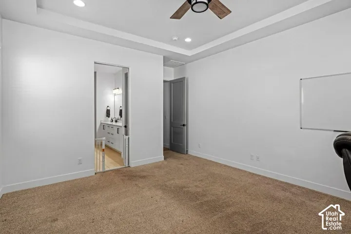 Tray ceiling with recessed lighting, ceiling fan with light fixture, carpeted flooring, and a gray interior door
