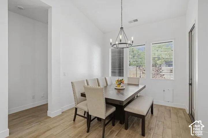 Vaulted ceiling with a chandelier, wood-finish flooring, multiple windows with blinds, and white walls