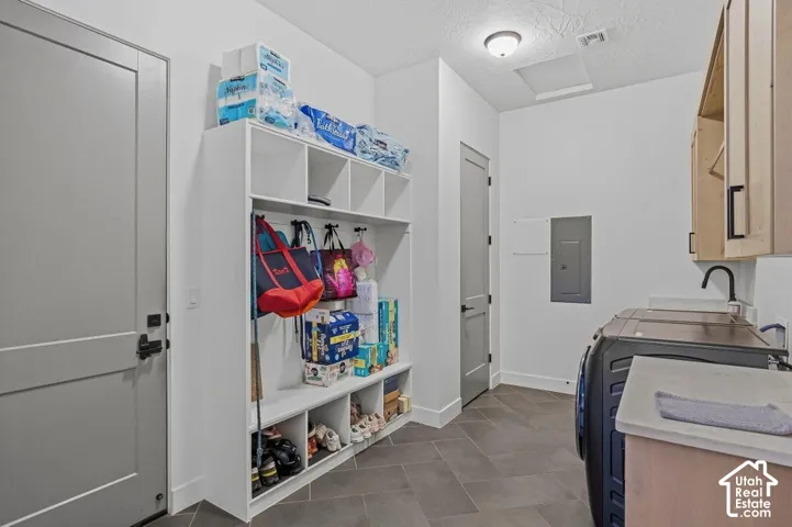 Built-in cubbies and shelving, dark gray tile flooring, light wood-finish cabinetry with black hardware, and an attached utility sink with a black faucet
