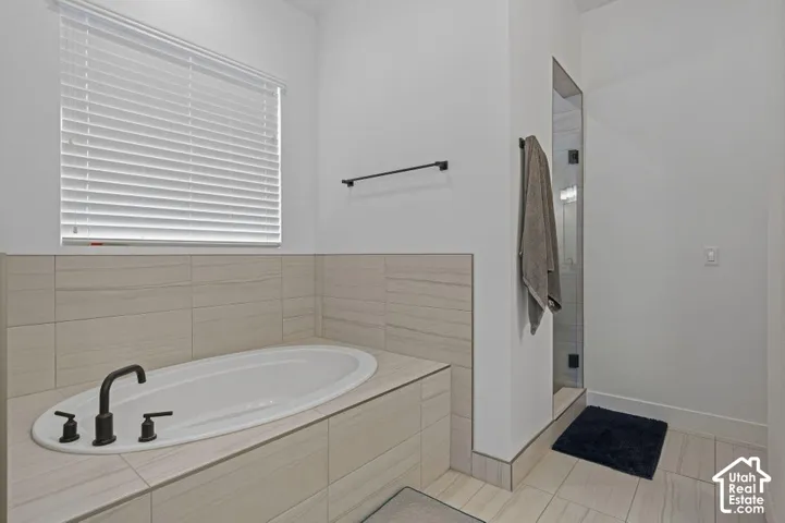 Recessed soaking tub with matte black fixtures, tiled surround, and separate glass-enclosed shower