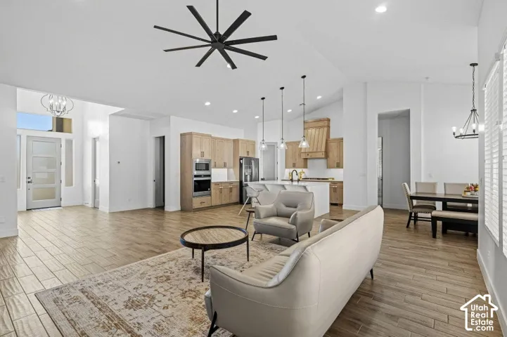 Vaulted ceiling with a contemporary ceiling fan, wood-finish flooring, and a kitchen featuring light wood cabinetry, stainless steel appliances, and an island with pendant lighting