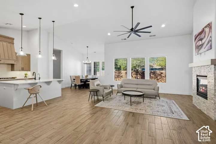 Spacious open-concept living area featuring wood-finish flooring, a stone-clad fireplace, and a contemporary ceiling fan