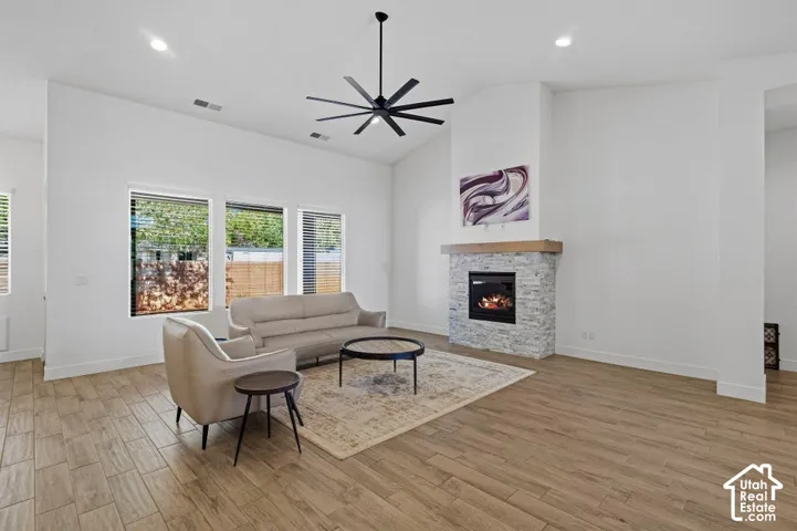 Vaulted ceiling with a black ceiling fan, wood-finish flooring, and a stone-clad fireplace with a wood mantel