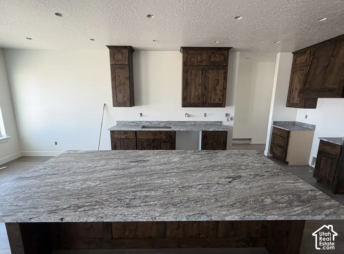 Spacious kitchen featuring an expansive island with a patterned countertop, recessed lighting, and rich wood cabinetry