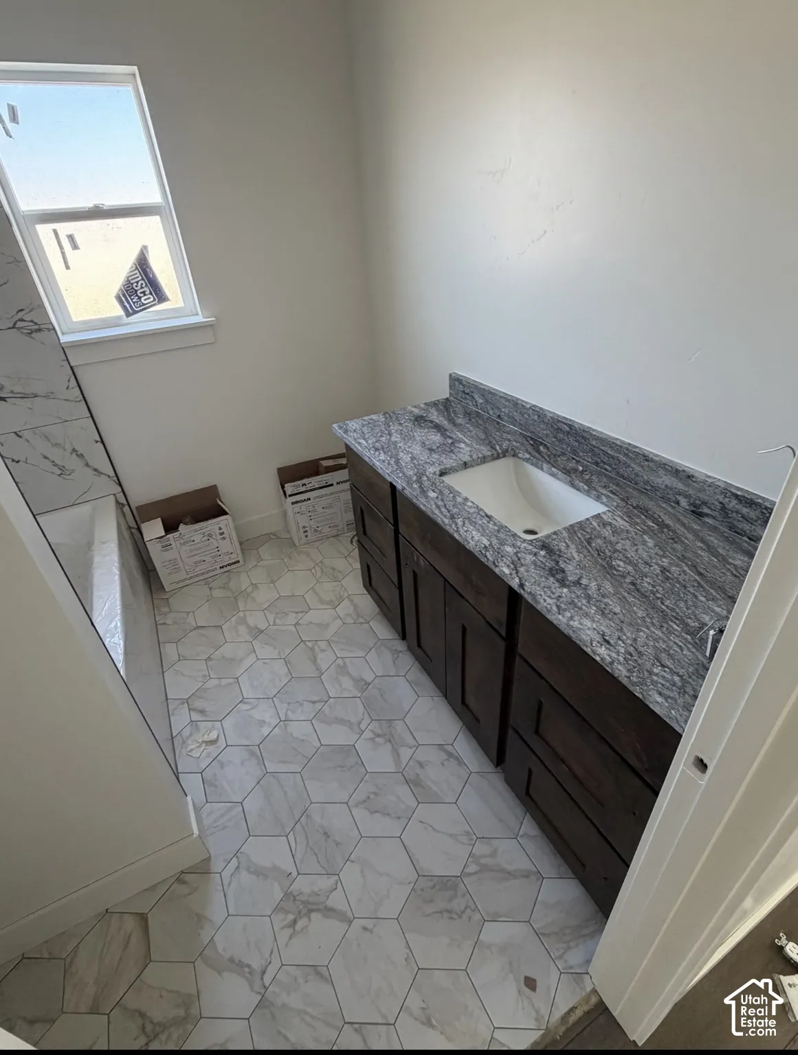 Hexagonal tile flooring, dark wood-finish vanity with ample storage, integrated basin sink, and a stone-finish countertop