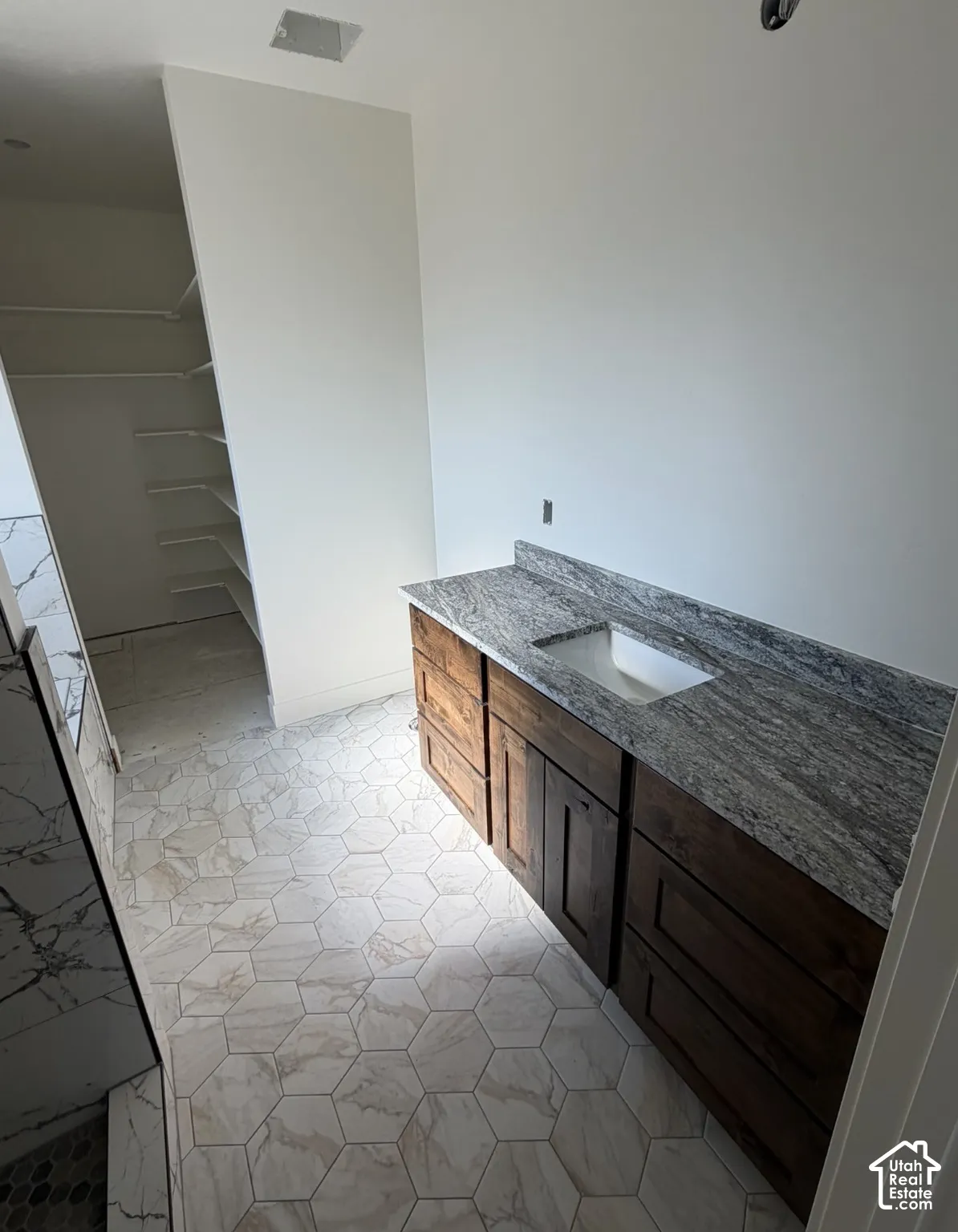 Hexagonal floor tiling, wood-finish vanity with ample storage, integrated basin, and stone-finish countertop
