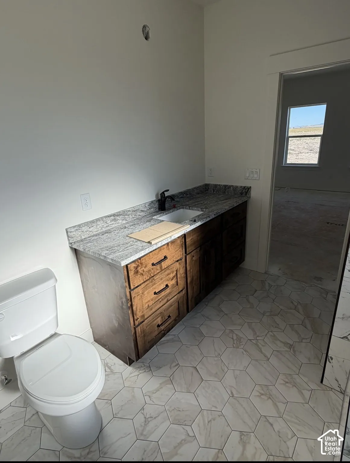 Hexagonal floor tiling, vanity with a rectangular sink, granite countertop, dark wood-finish cabinetry, and a black faucet