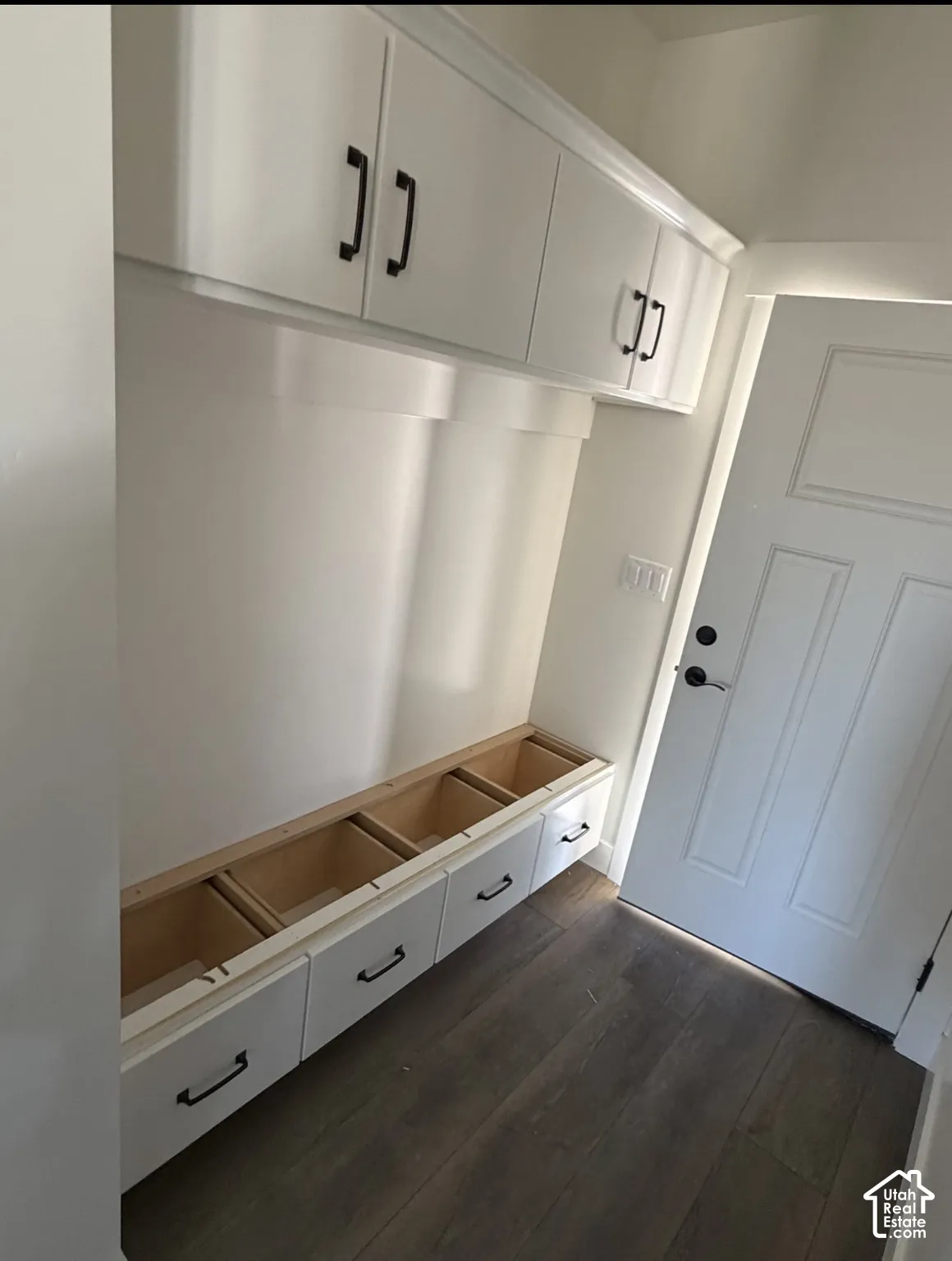 Built-in white cabinetry with matte black hardware, integrated bench seating with drawer storage, and dark wood-finish flooring