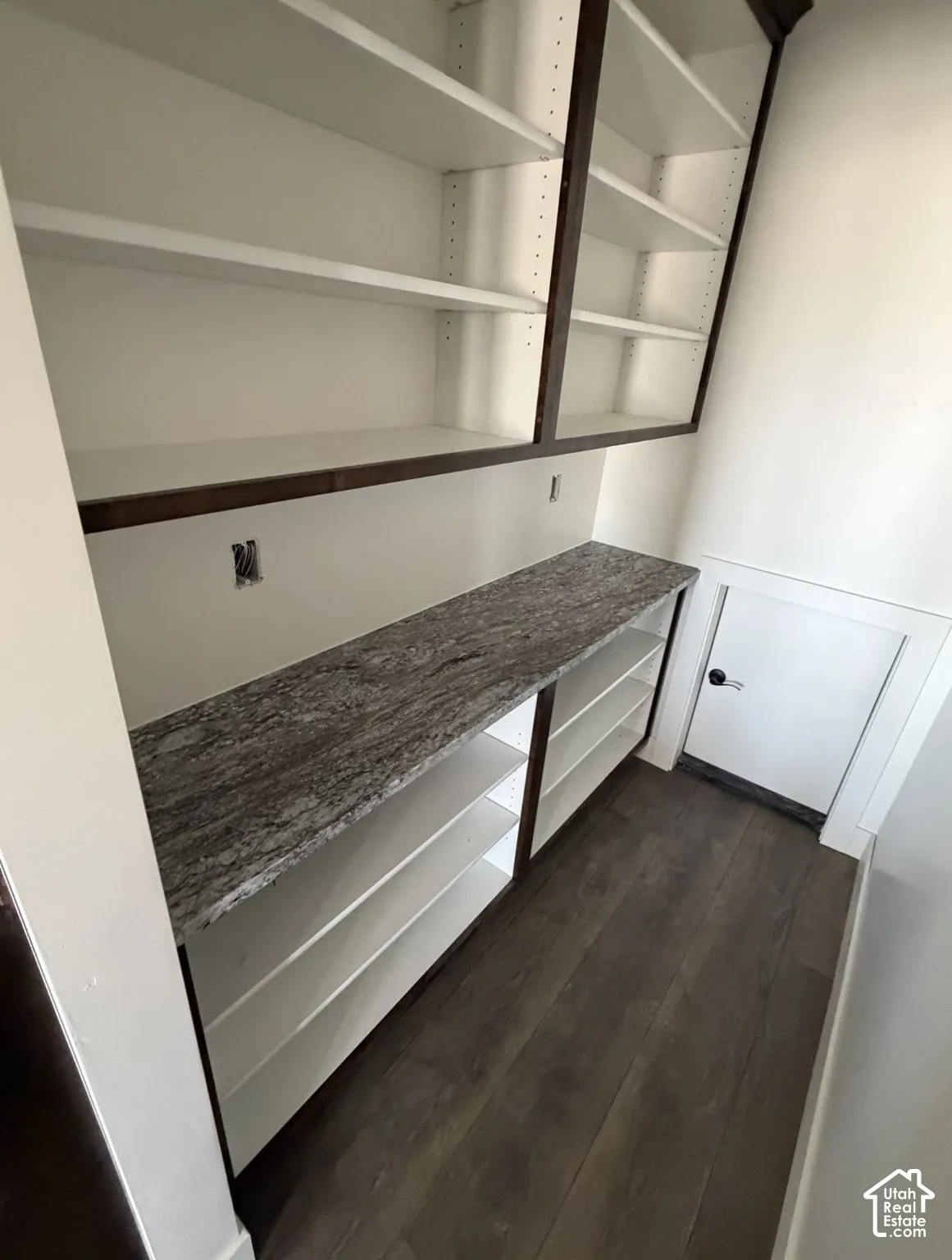 Built-in shelving with dark wood-finish framing, white adjustable shelves, a stone-finish countertop, and wood-finish flooring