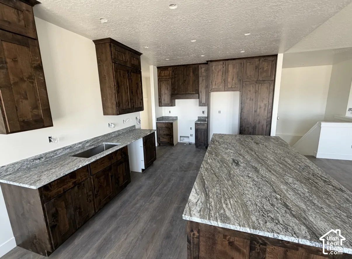 Kitchen featuring extensive dark wood-finish cabinetry, a large center island with a stone countertop, perimeter stone countertops, and wood-finish flooring
