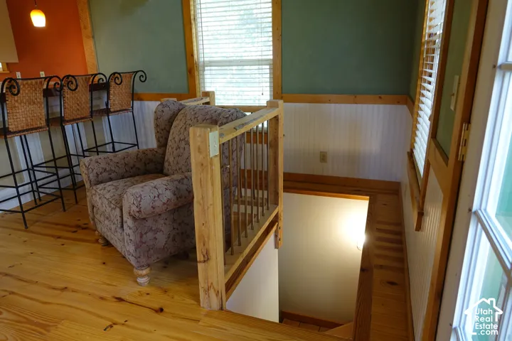 Wood-finish flooring, wood staircase with railing, beadboard wainscoting, and windows with blinds