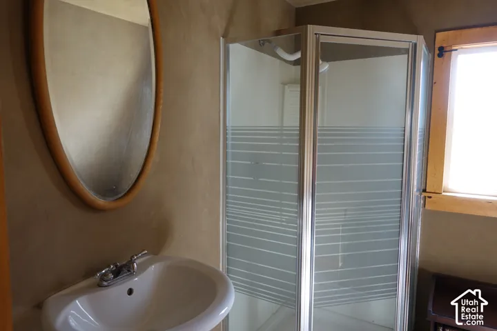 Pedestal sink with chrome faucet, framed oval mirror, and enclosed shower with frosted panels