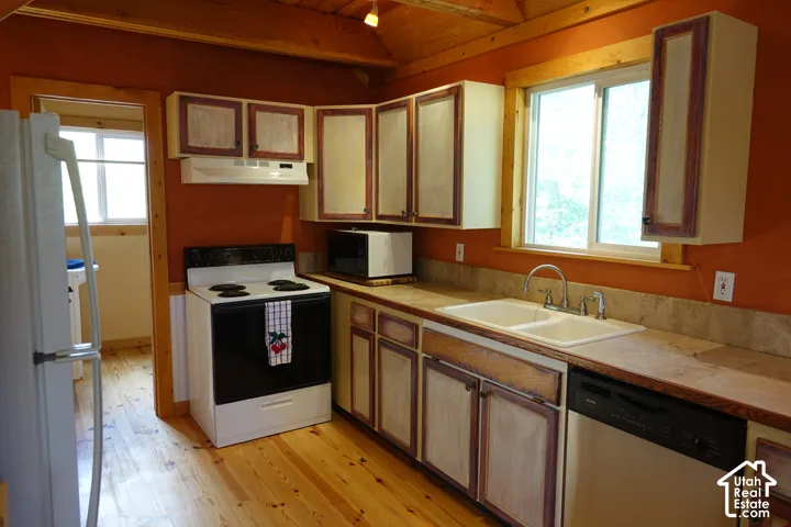 Kitchen featuring wood flooring, wood-beamed ceiling, built-in cabinetry, dual basin sink with chrome faucet, and a window with blinds