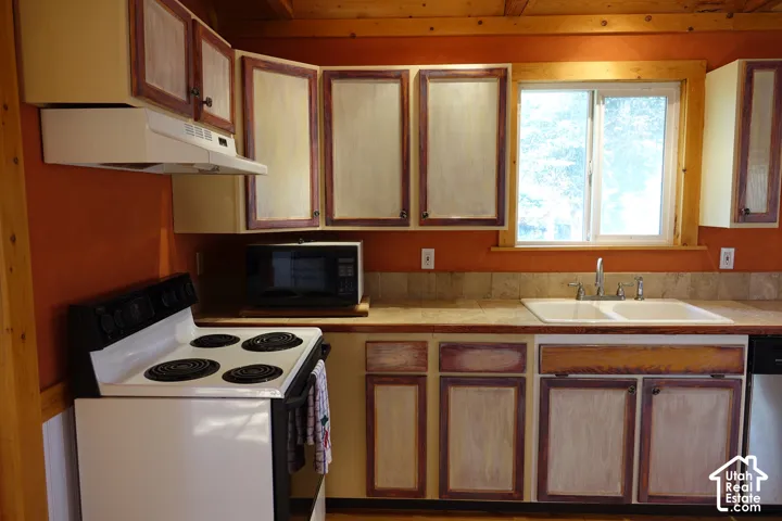 Kitchen featuring wood-finish cabinetry, tile countertops, a double basin sink, and a window with wood trim