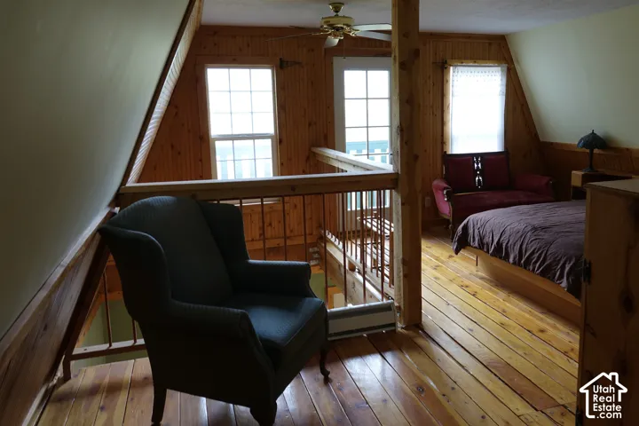Wood flooring throughout, beadboard wall paneling, pitched ceiling with a ceiling fan, and multiple windows providing natural illumination