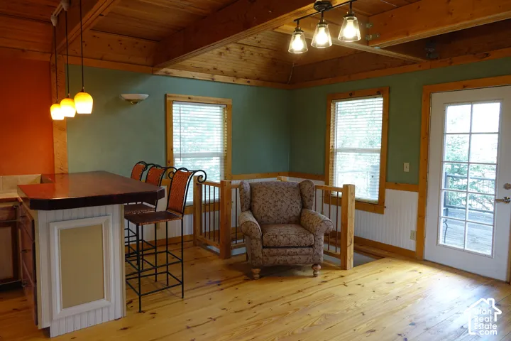 Wood flooring, exposed wood beam ceiling, wood-top breakfast bar, white paneled lower walls, and a multi-pane glass door