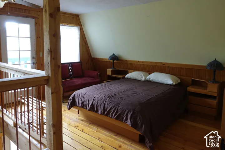 Wood flooring, wood paneling, sloped ceiling, wood headboard with wood nightstands, and a glass-paned door