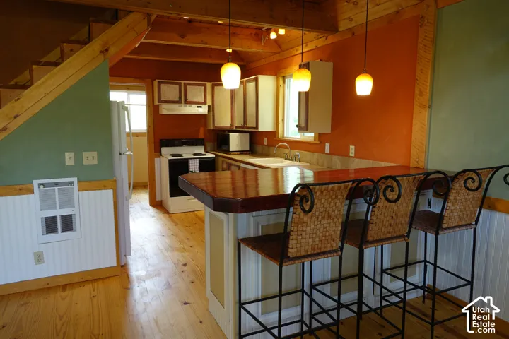 Kitchen featuring a wood peninsula with pendant lighting, white and brown two toned raised cabinetry, wood flooring, and exposed wood beams