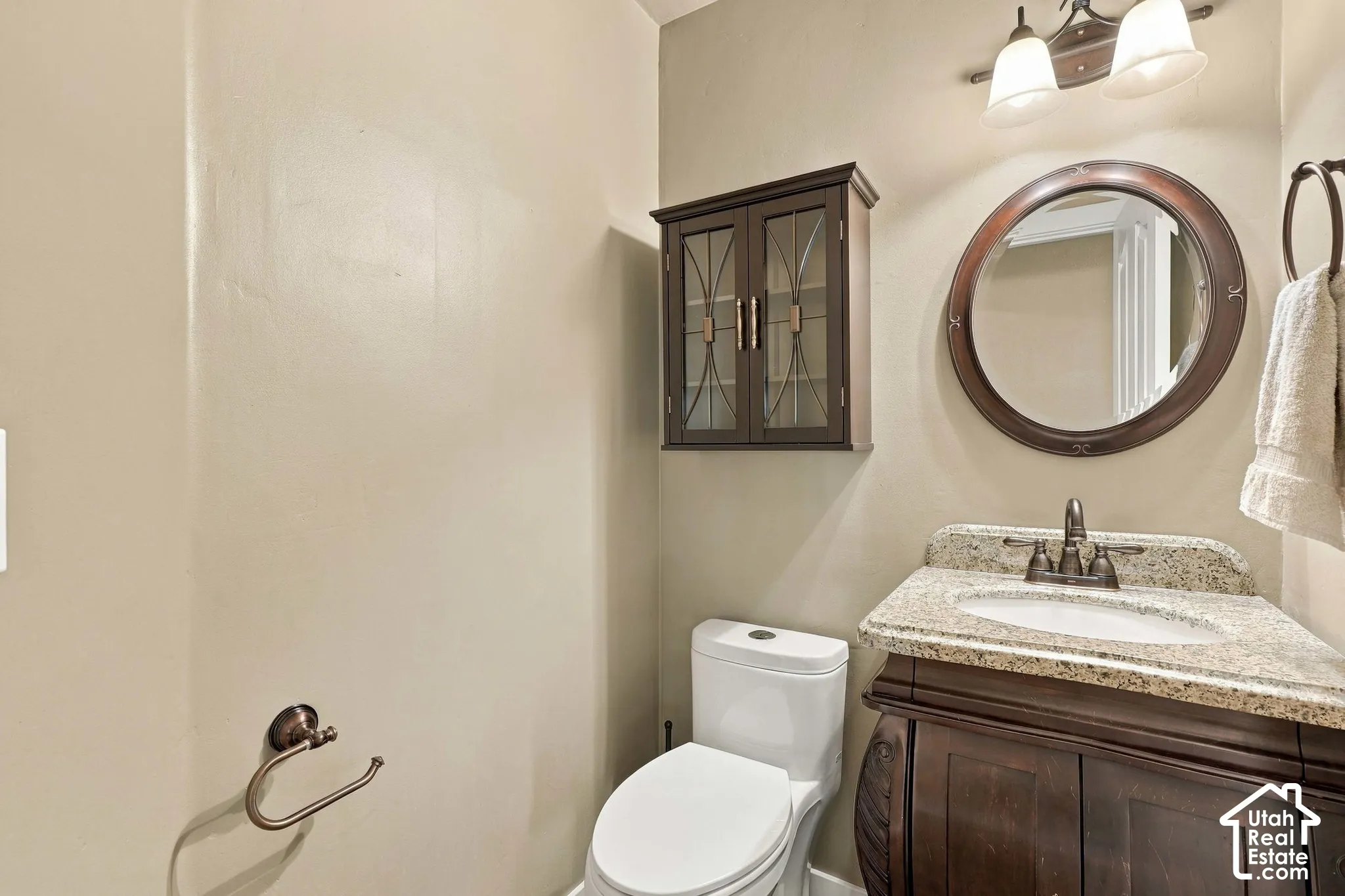 Vanity with stone countertop, round mirror, dark wood cabinetry, and wall-mounted light fixture