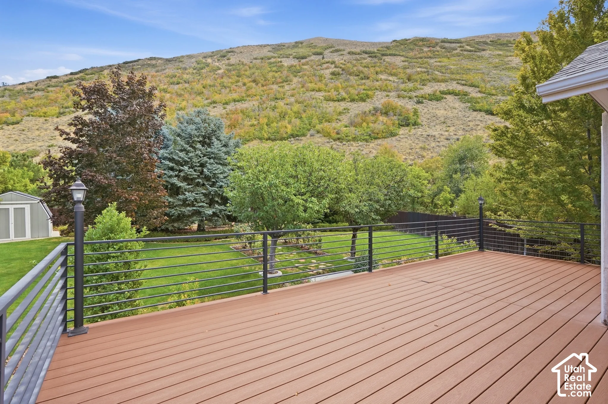 Spacious deck featuring composite decking and black metal railings, overlooking a grassy yard with mature trees and a distant hillside
