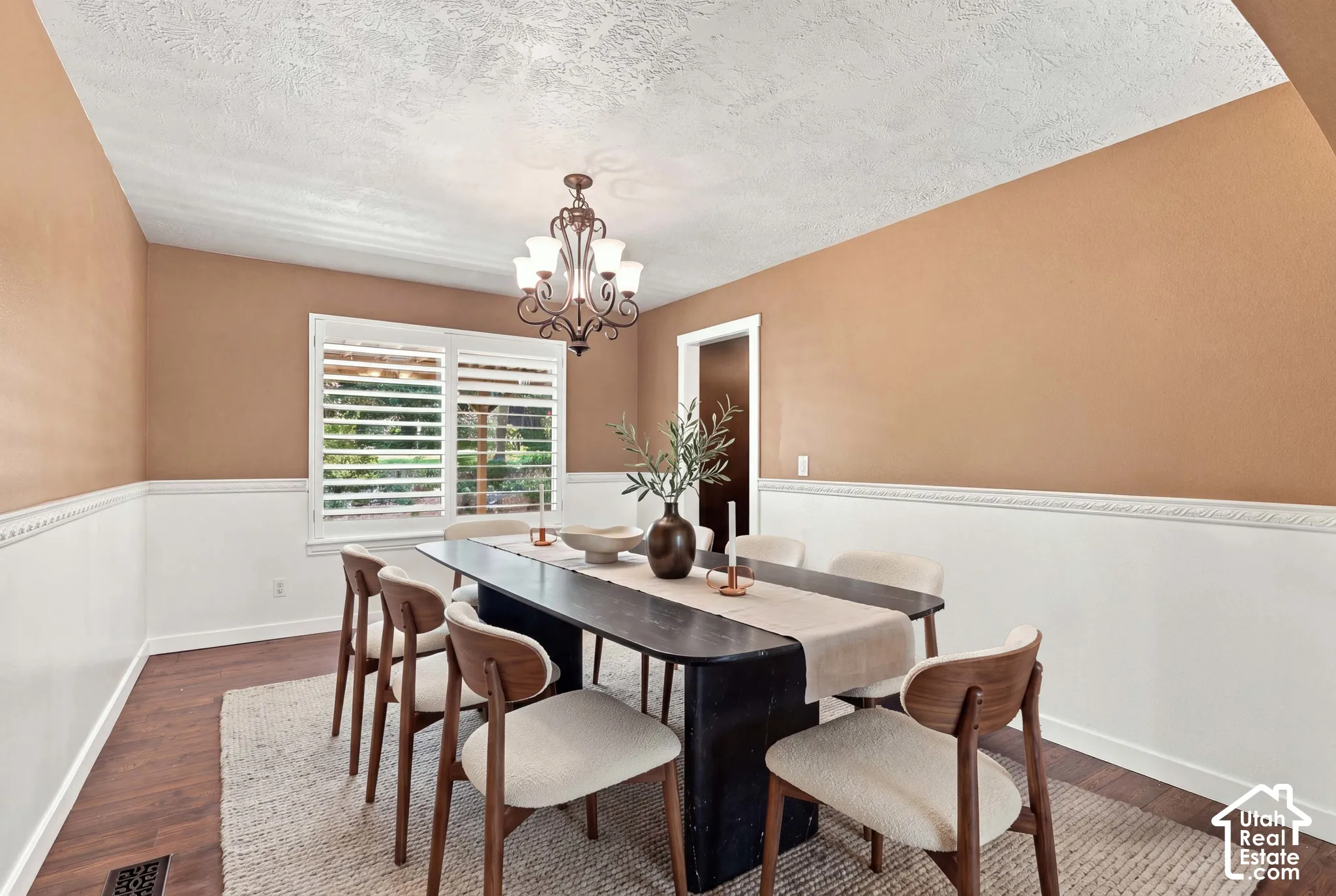Dining area featuring wood-finish flooring, white wainscoting with decorative trim, a window with plantation shutters, and a chandelier