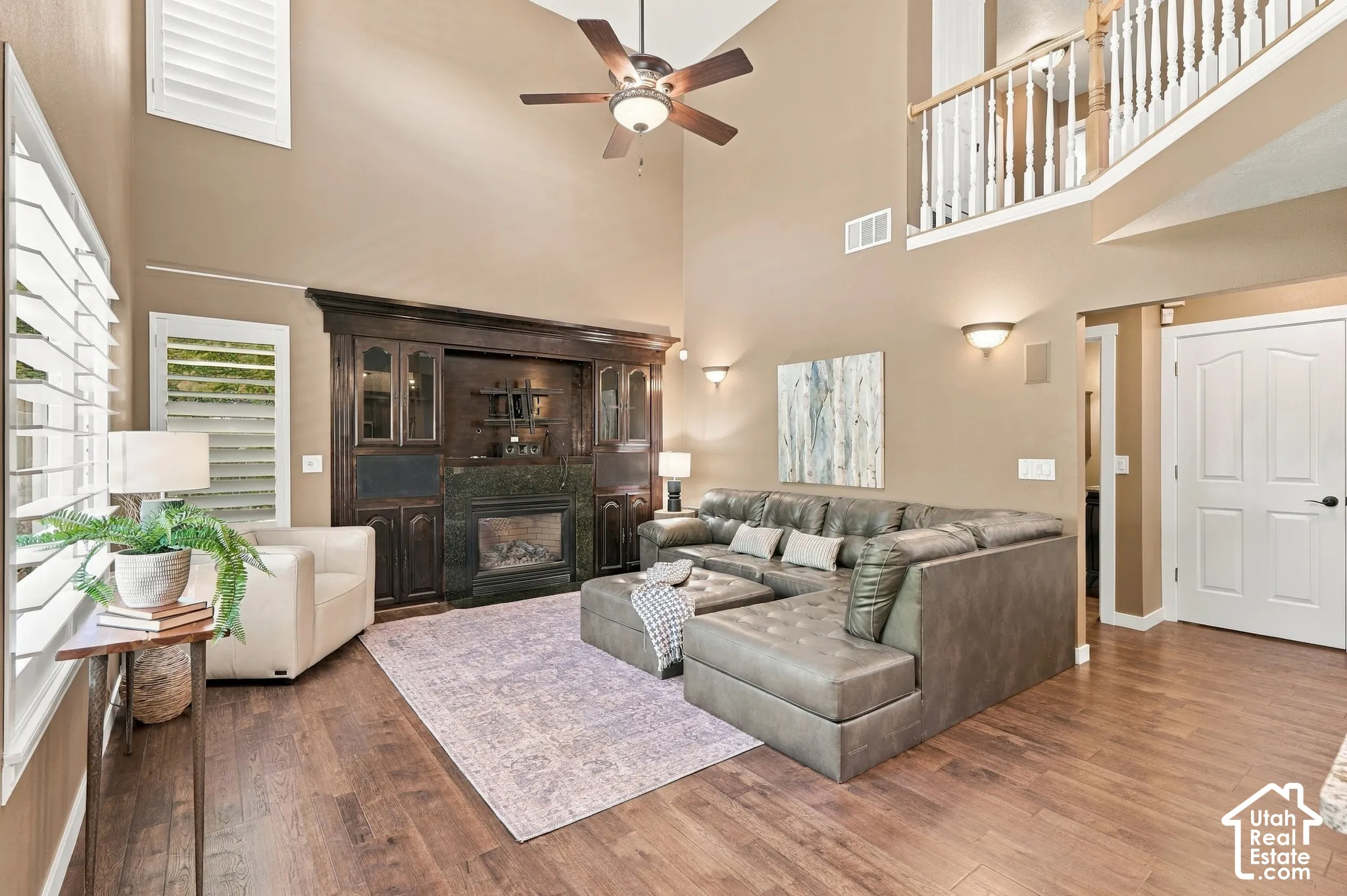 Vaulted living room featuring wood-finish flooring, a built-in entertainment center with a fireplace, and a ceiling fan