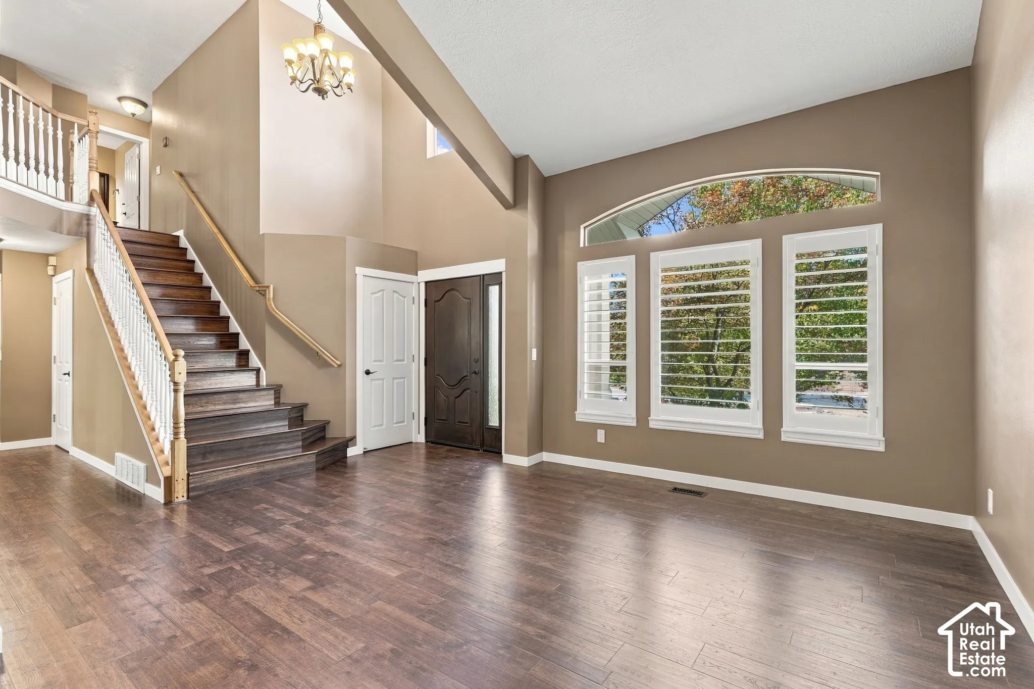 Vaulted ceilings with a decorative chandelier, expansive wood-finish flooring, and a grand staircase with white balusters