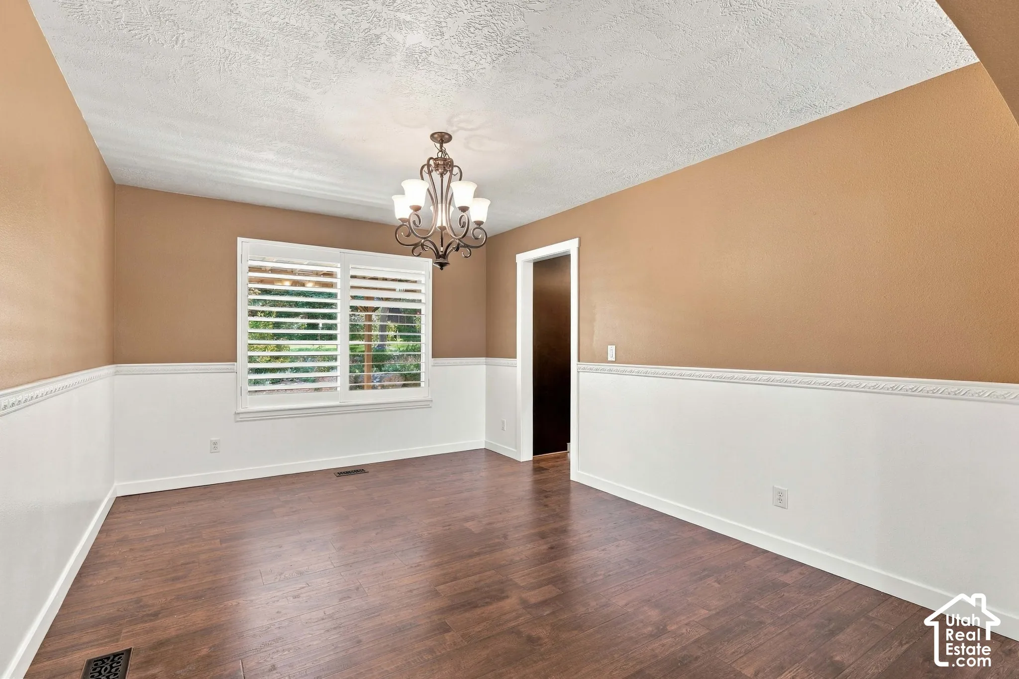 Wood-finish flooring, white wainscoting, and a decorative chandelier