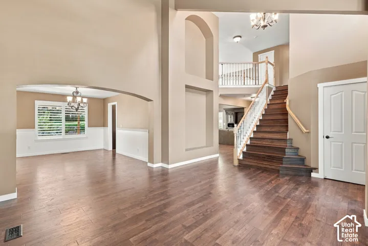 Hardwood-finish flooring throughout, grand staircase with white balusters, arched doorways, two-story entryway, and a chandelier lighting fixture