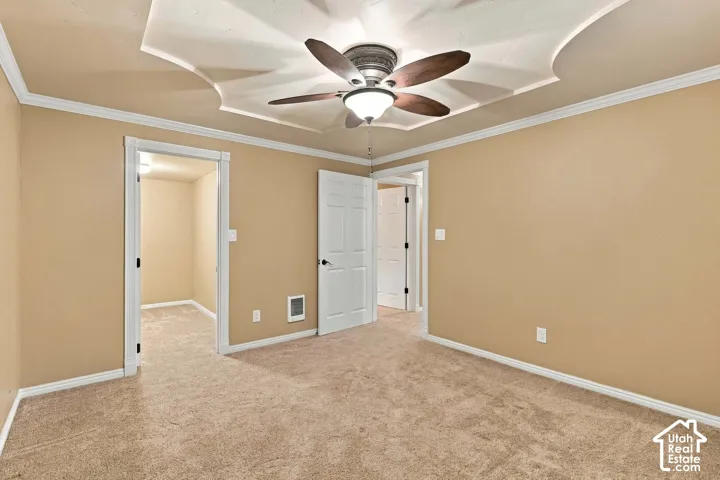 Tray ceiling with crown molding, ceiling fan with integrated lighting, textured carpeting, and painted walls