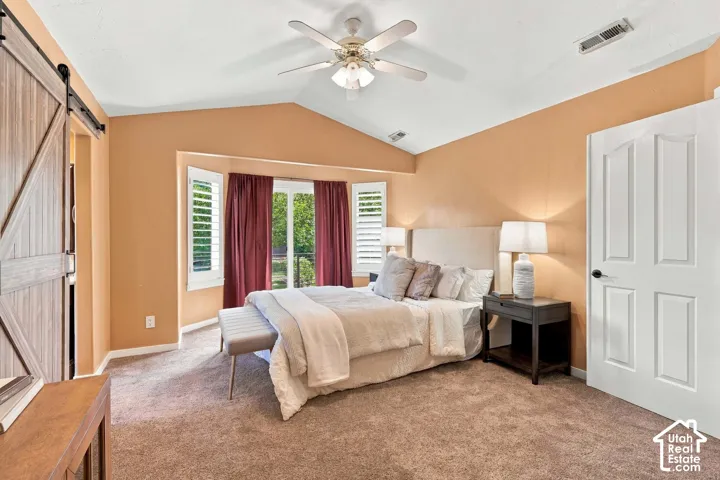 Angled vaulted ceiling with a ceiling fan, a barn door, and carpet flooring