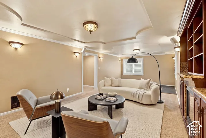 Recessed ceiling with decorative molding, wall sconces, built-in cabinetry with shelving, window with plantation shutters, and carpet flooring
